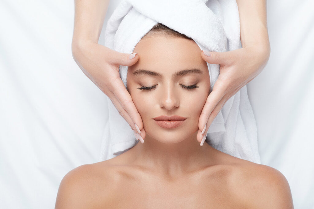 Young girl with thick eyebrows and perfect skin at white background, towel on head, beauty photo concept, skin care, spa concept, treatment, face massage.