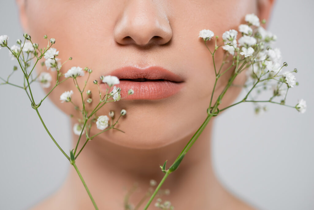 close up view of cropped female face near white gypsophila flowers isolated on grey. 